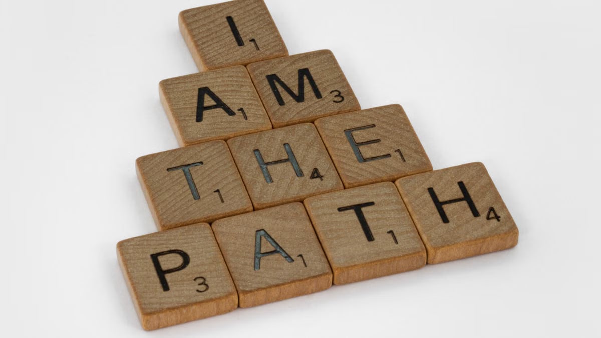 Scrabble tiles arranged to form the quote 'I am the path' on a white surface.